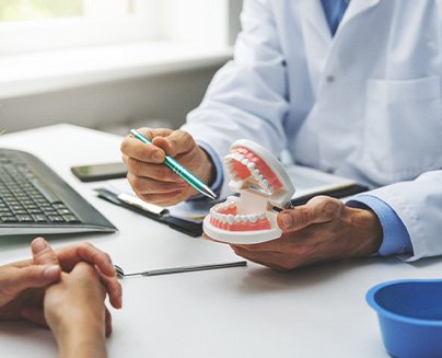 a dentist speaking with a patient about dentures and showing them a model of a mouth